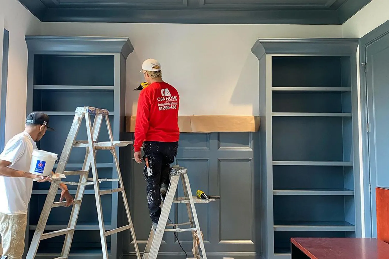 C&A painter finishing blue built-in bookcases in a living room